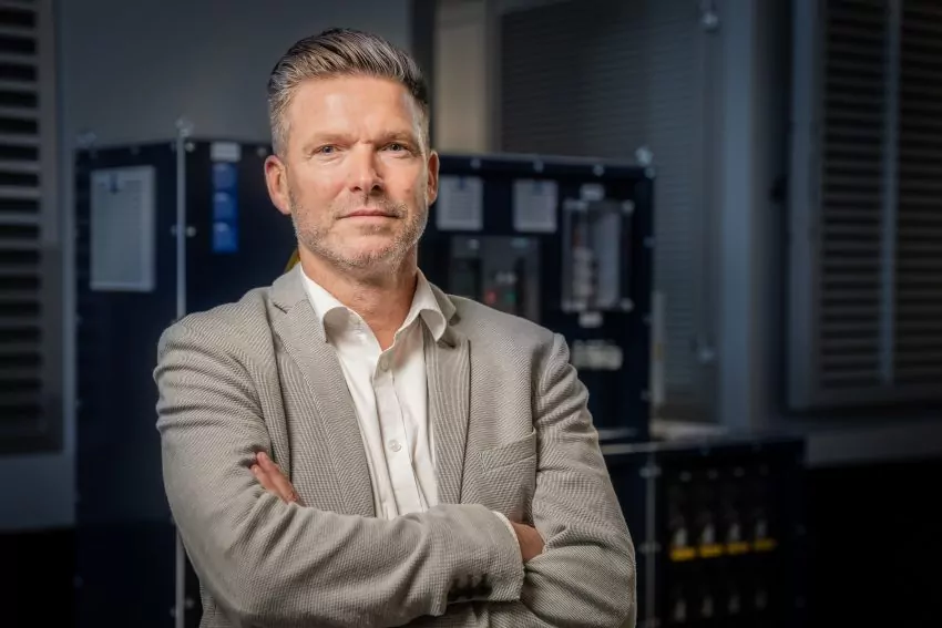Portret van een man in een grijs colbert met gekruiste armen voor een schakelinstallatie