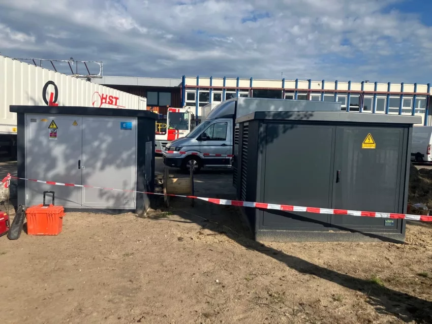 Twee nieuw geplaatste transformatorstations met waarschuwingsstickers, afgezet met lint