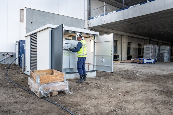 Monteur werkt in een geopend transformatorstation naast een bouwproject